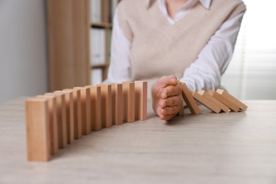 Photo of Woman stopping wooden blocks from falling at table, closeup. Domino effect