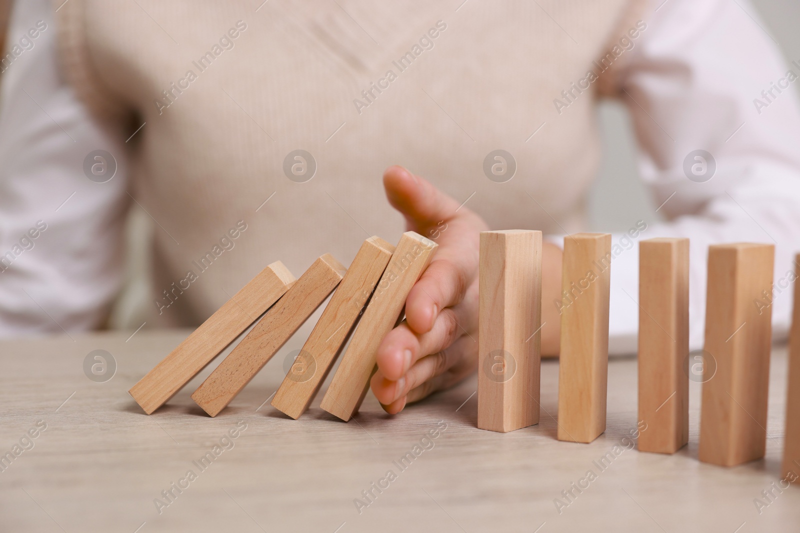 Photo of Woman stopping wooden blocks from falling at table, closeup. Domino effect