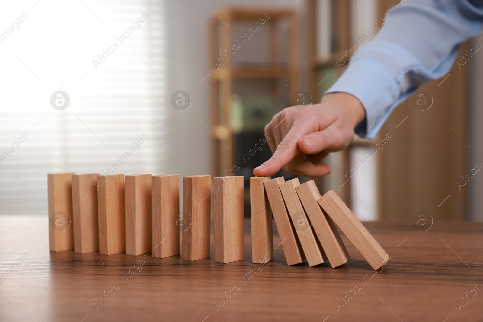 Photo of Woman stopping wooden blocks from falling at table, closeup. Domino effect