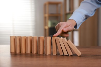 Photo of Woman stopping wooden blocks from falling at table, closeup. Domino effect