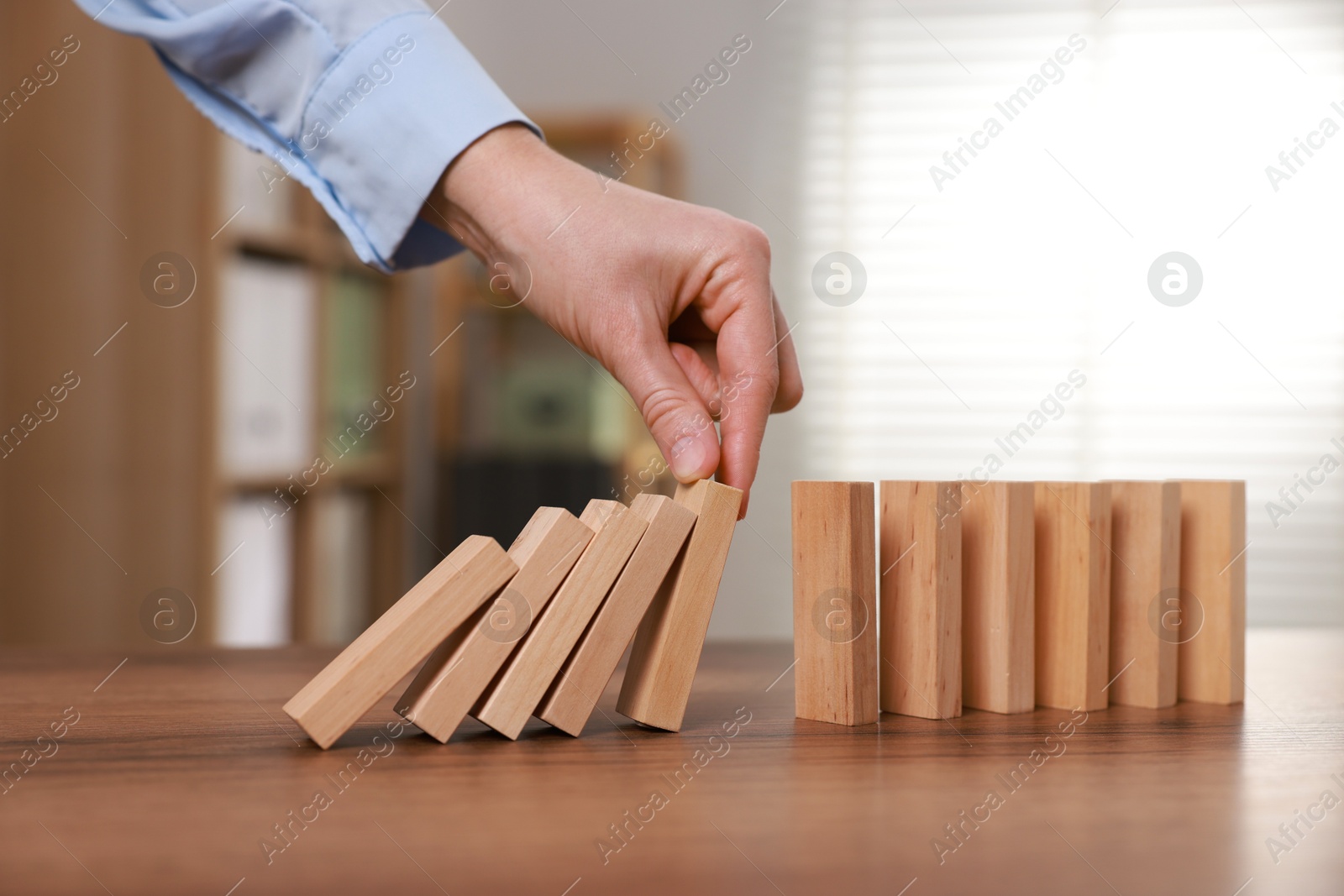 Photo of Woman stopping wooden blocks from falling at table, closeup. Domino effect