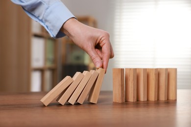 Photo of Woman stopping wooden blocks from falling at table, closeup. Domino effect