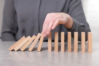 Photo of Woman stopping wooden blocks from falling at table, closeup. Domino effect