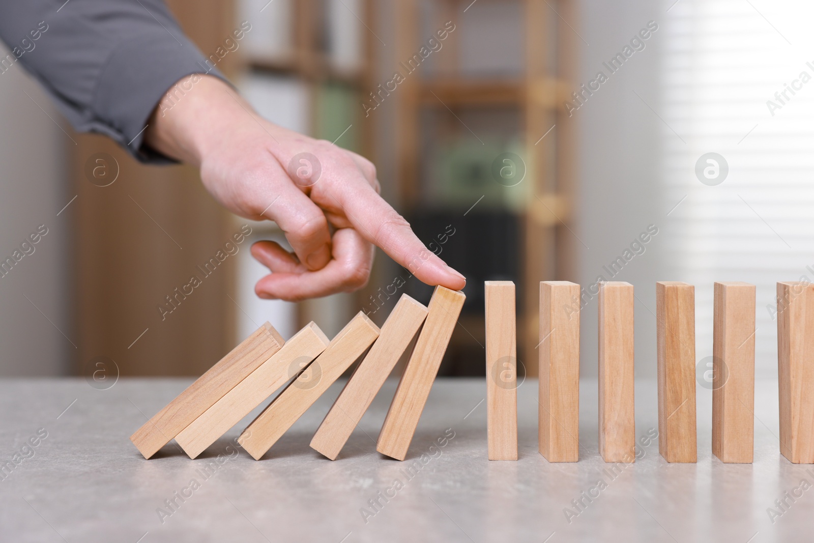 Photo of Woman stopping wooden blocks from falling at table, closeup. Domino effect