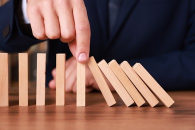 Photo of Man stopping wooden blocks from falling at table, closeup. Domino effect