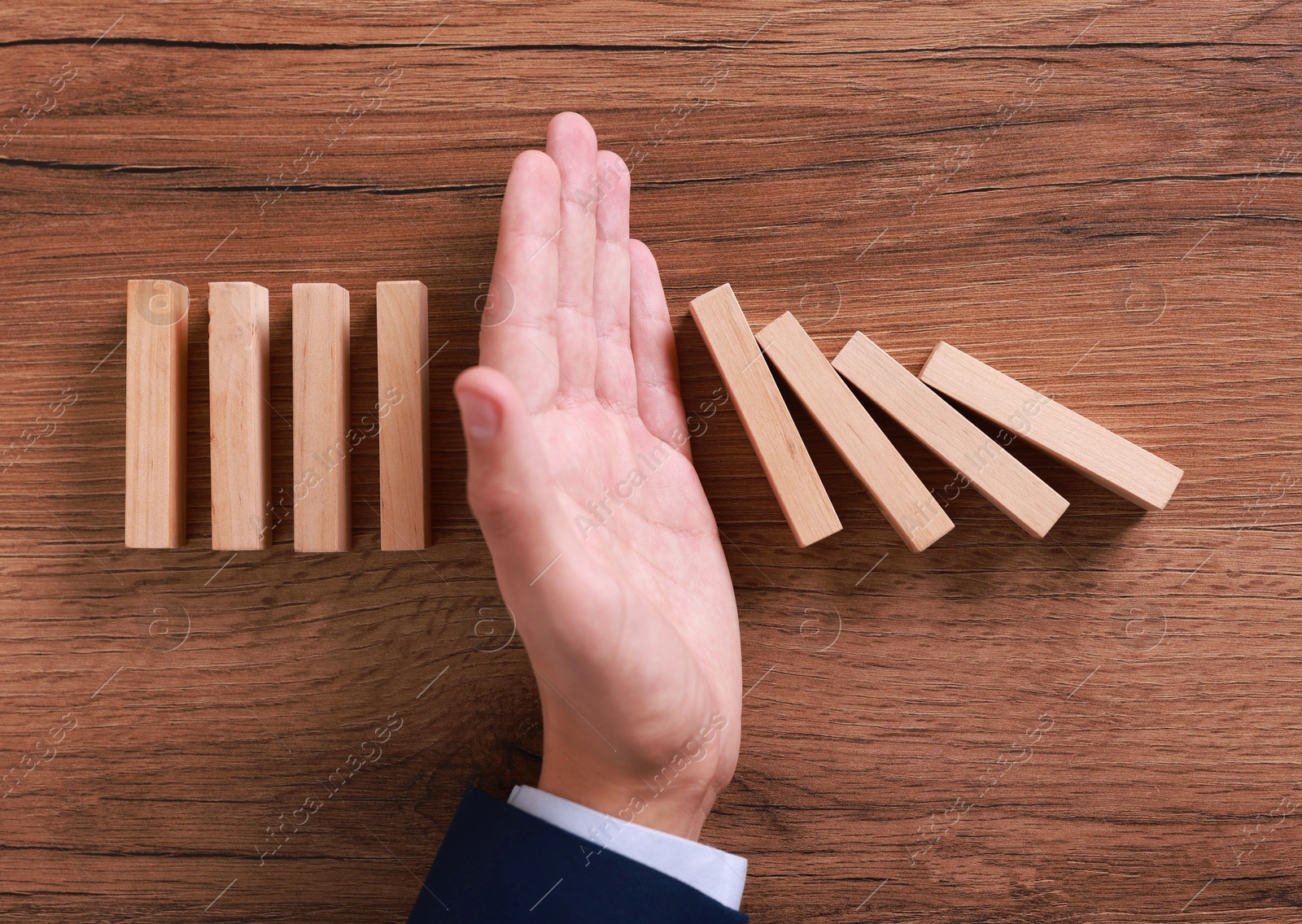 Photo of Man stopping wooden blocks from falling at table, top view. Domino effect