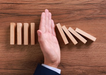 Photo of Man stopping wooden blocks from falling at table, top view. Domino effect