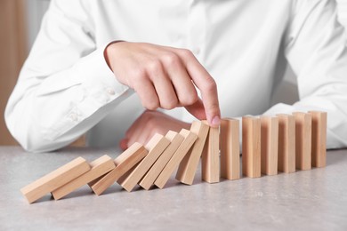 Photo of Man stopping wooden blocks from falling at table, closeup. Domino effect