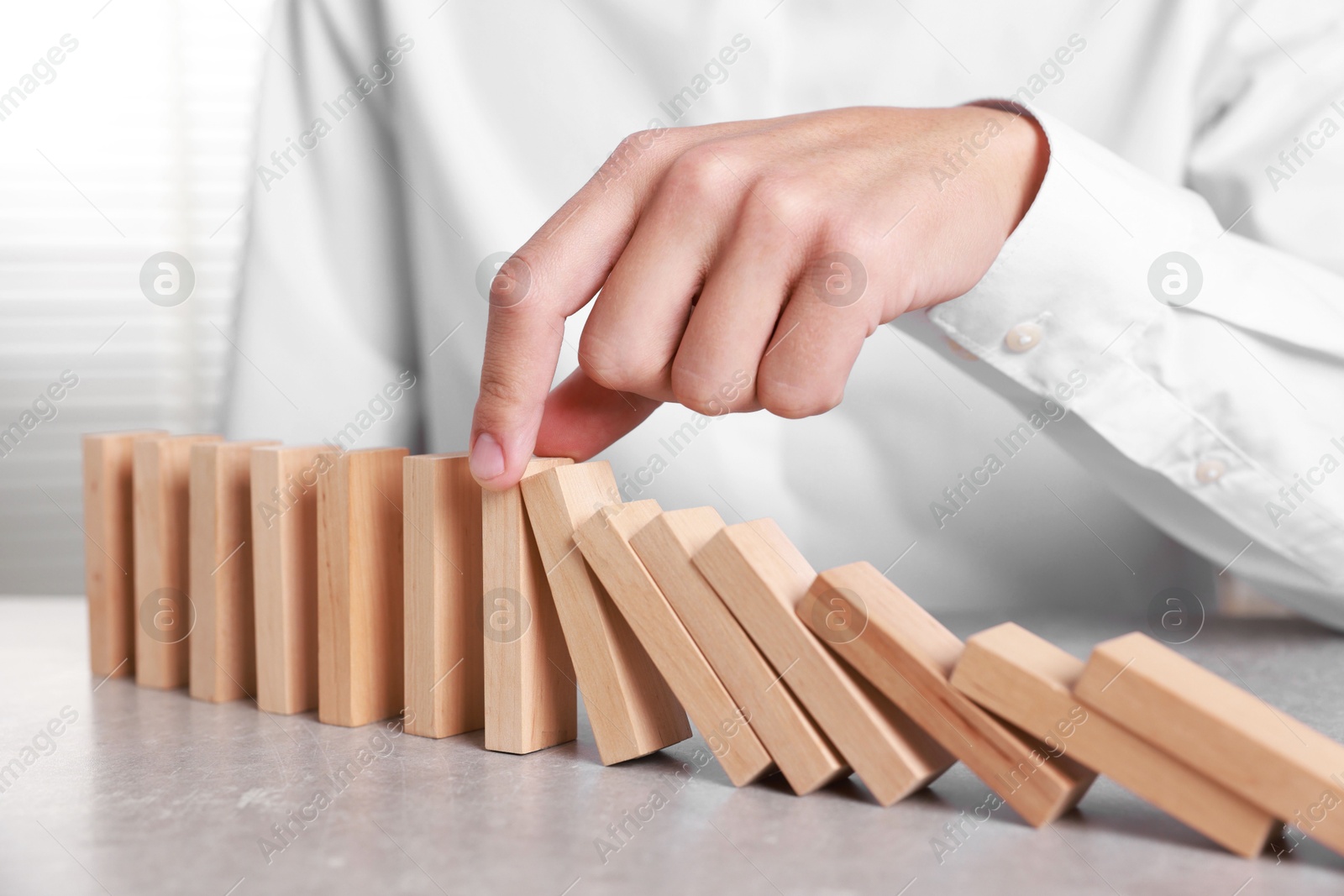 Photo of Man stopping wooden blocks from falling at table, closeup. Domino effect