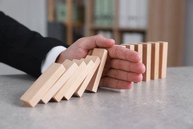 Photo of Man stopping wooden blocks from falling at table, closeup. Domino effect