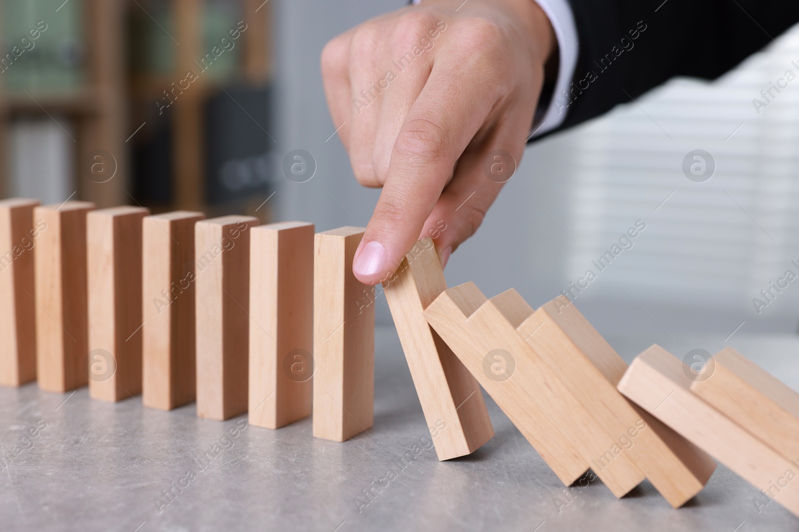 Photo of Man stopping wooden blocks from falling at table, closeup. Domino effect