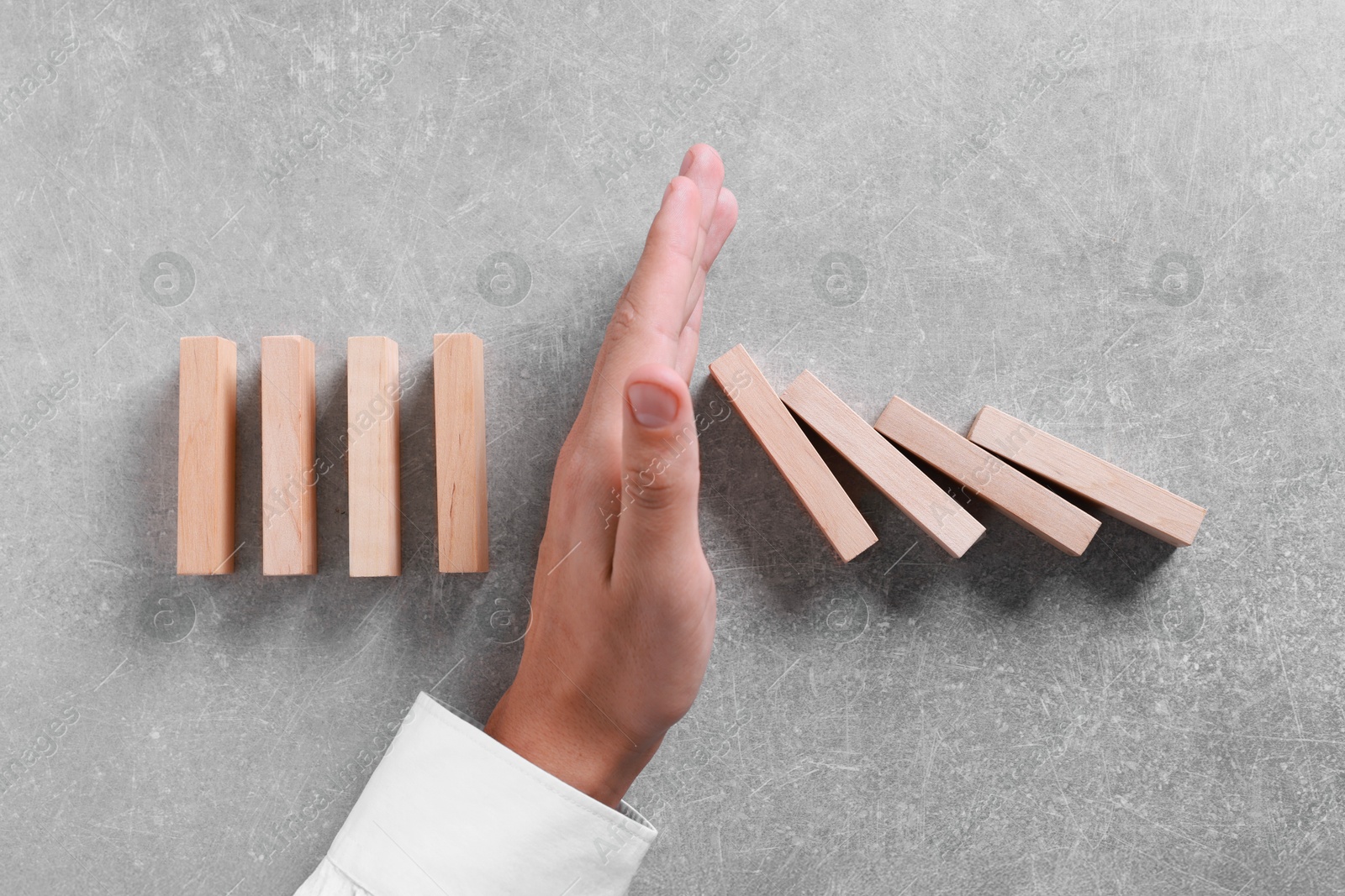 Photo of Man stopping wooden blocks from falling on grey background, top view. Domino effect