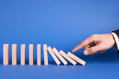 Photo of Domino effect. Man pushing wooden blocks on blue background, closeup