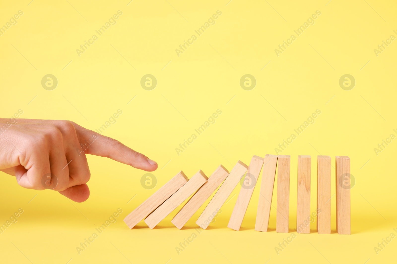 Photo of Domino effect. Man pushing wooden blocks on yellow background, closeup