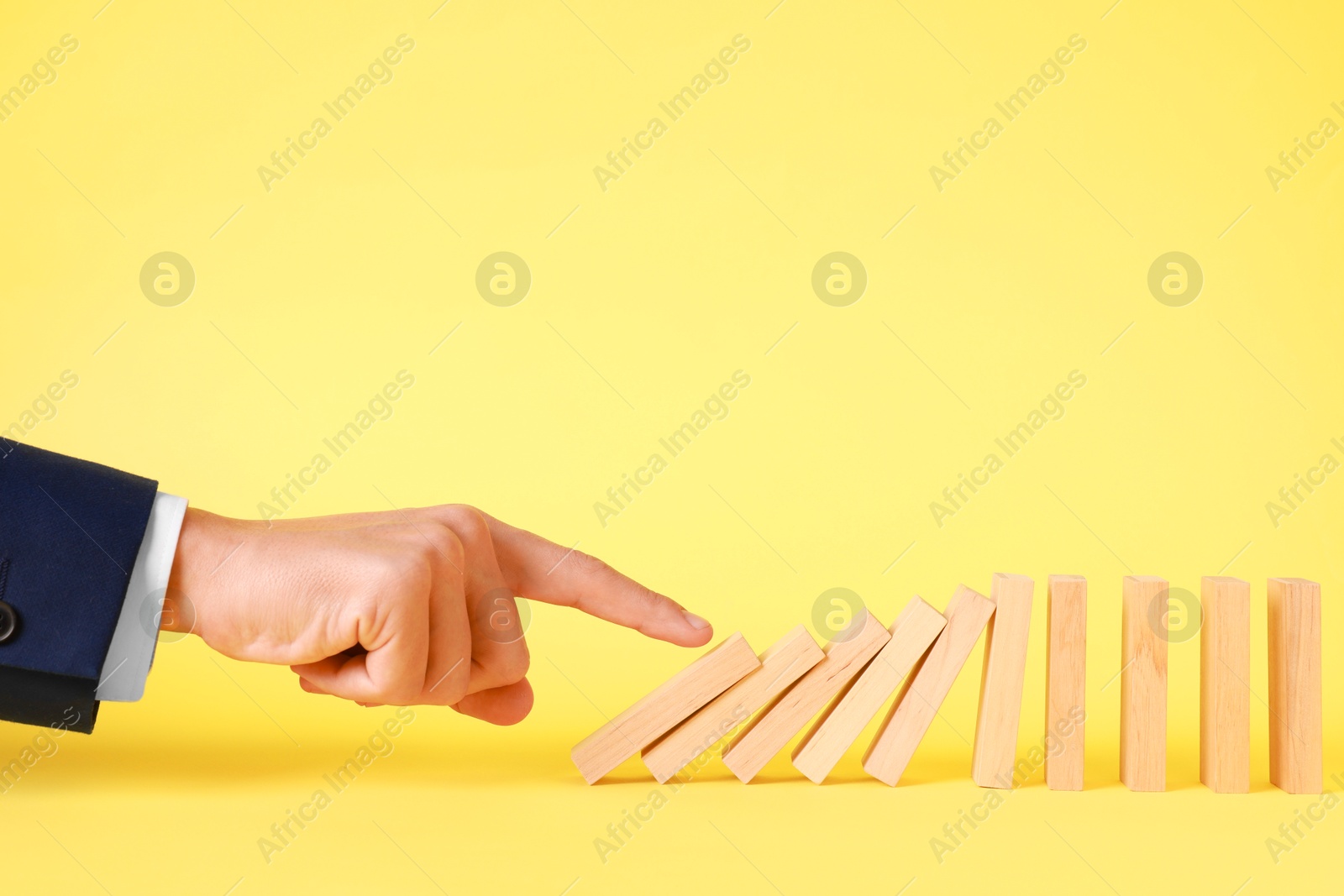 Photo of Domino effect. Man pushing wooden blocks on yellow background, closeup