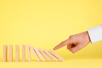 Photo of Domino effect. Man pushing wooden blocks on yellow background, closeup