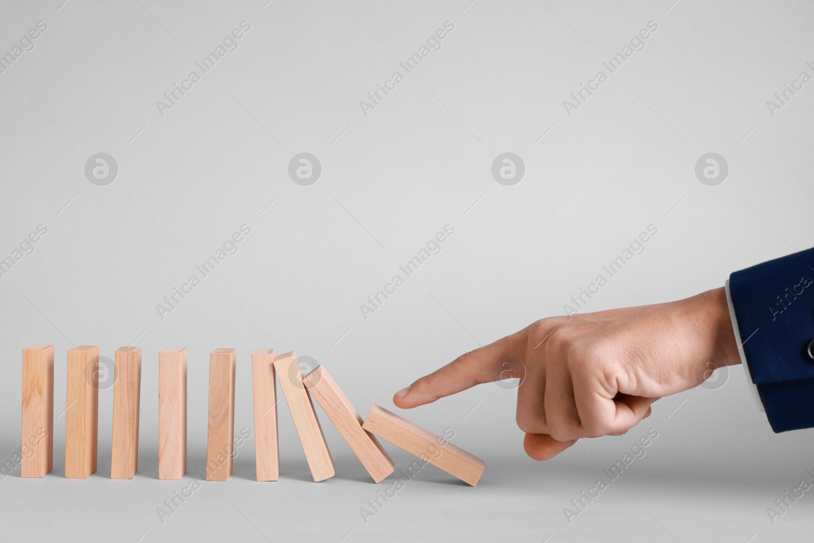 Photo of Domino effect. Man pushing wooden blocks on light background, closeup