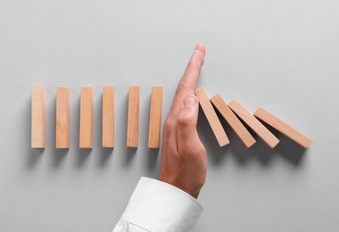 Photo of Man stopping wooden blocks from falling on grey background, top view. Domino effect