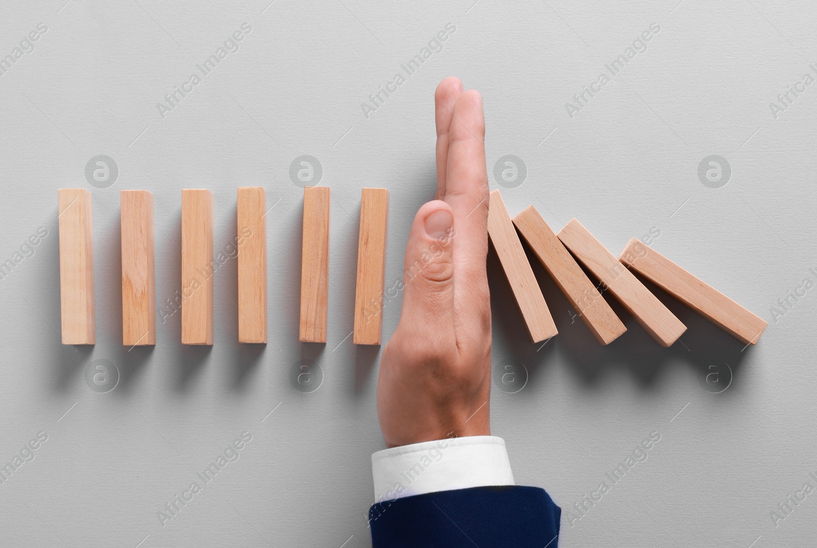 Photo of Man stopping wooden blocks from falling on grey background, top view. Domino effect