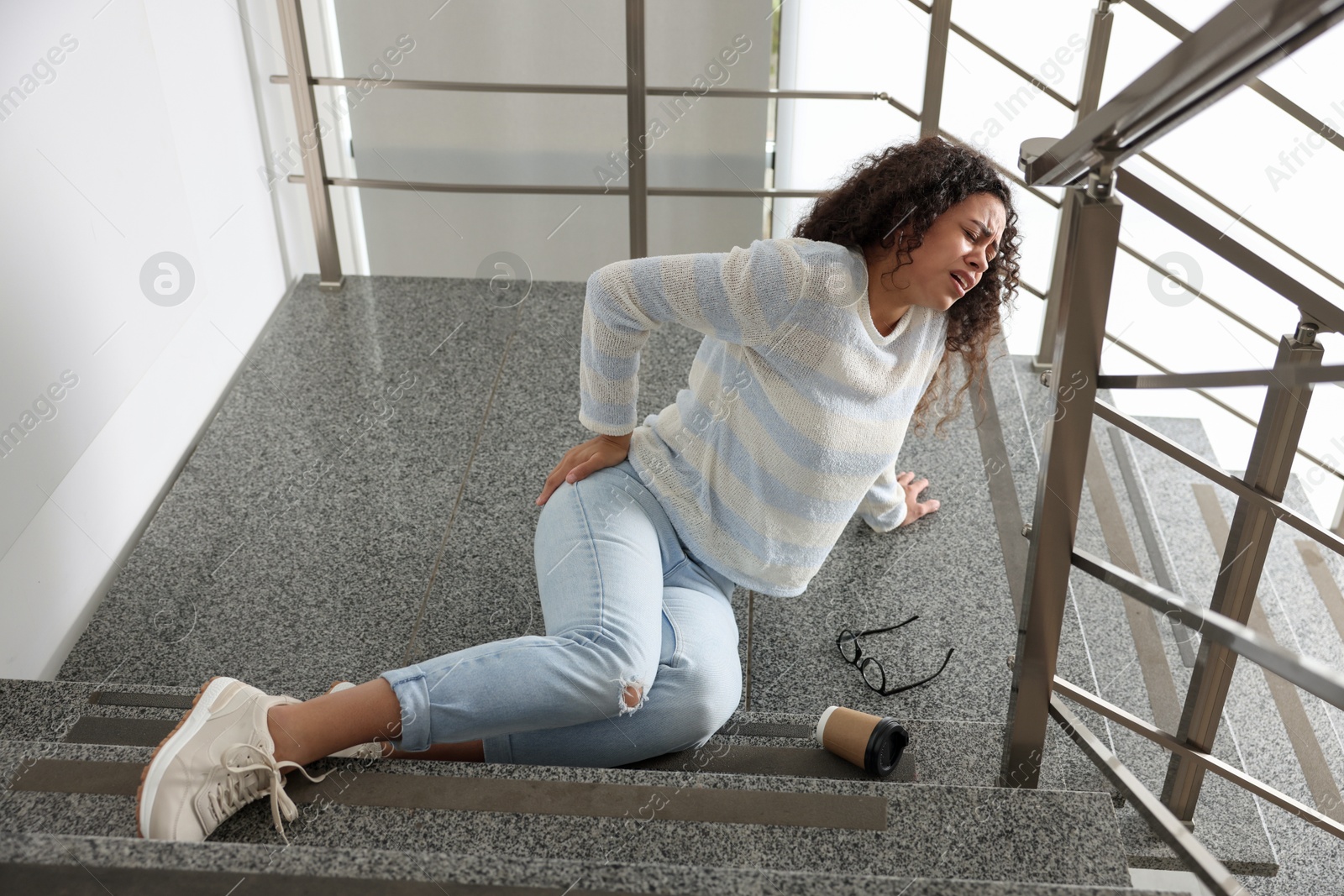 Photo of Woman with injured back on stairs in building after fall. Dangerous accident