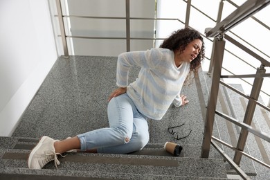 Photo of Woman with injured back on stairs in building after fall. Dangerous accident