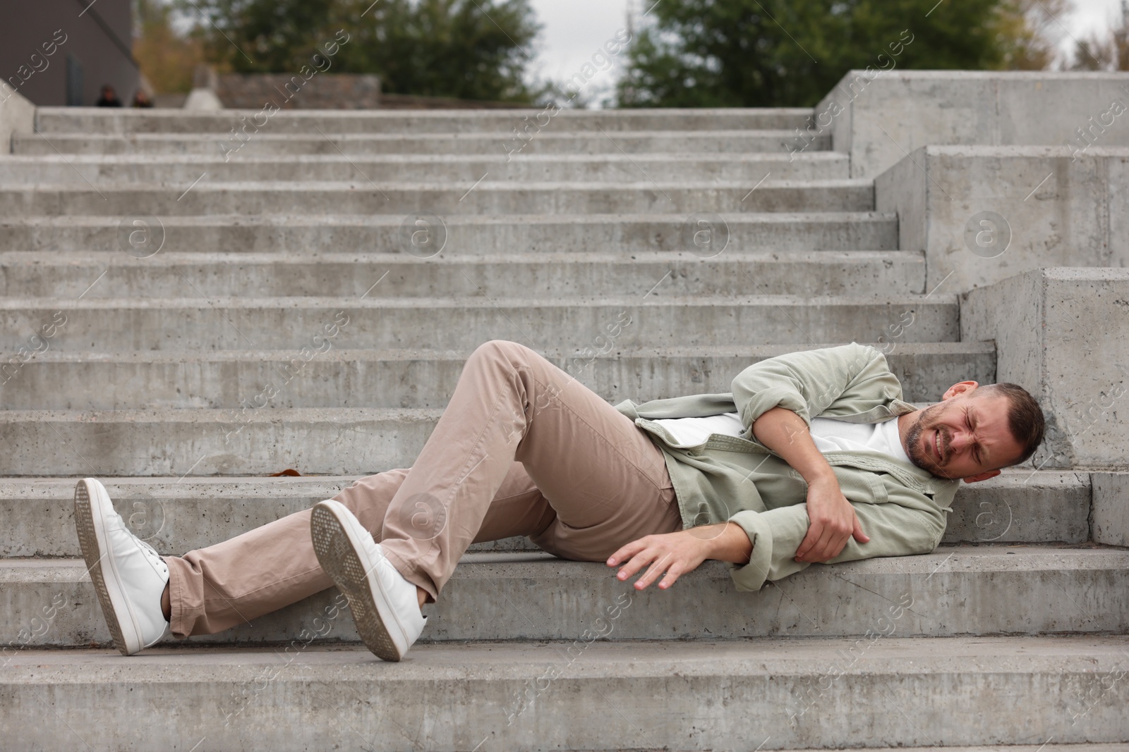 Photo of Man with injured arm on stairs outdoors after fall. Dangerous accident