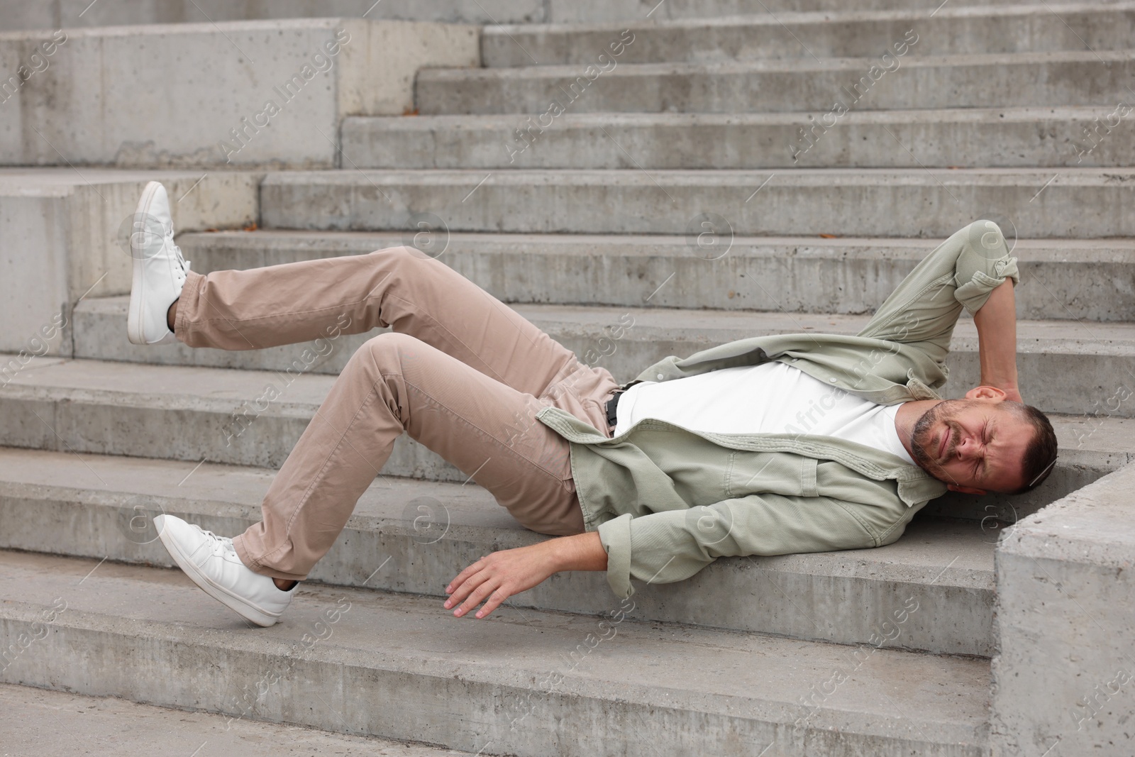 Photo of Man with injured head on stairs outdoors after fall. Dangerous accident