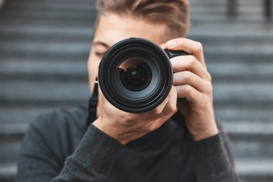 Photo of Professional photographer taking picture with camera outdoors, selective focus