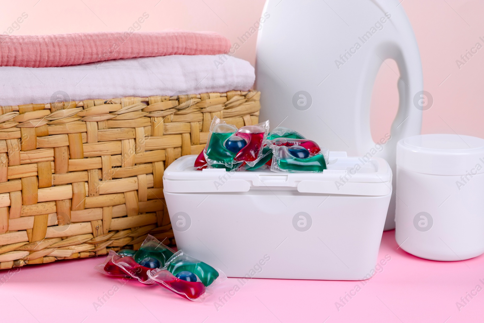 Photo of Laundry capsules, detergent and clean linens on pink table, closeup