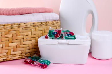 Photo of Laundry capsules, detergent and clean linens on pink table, closeup