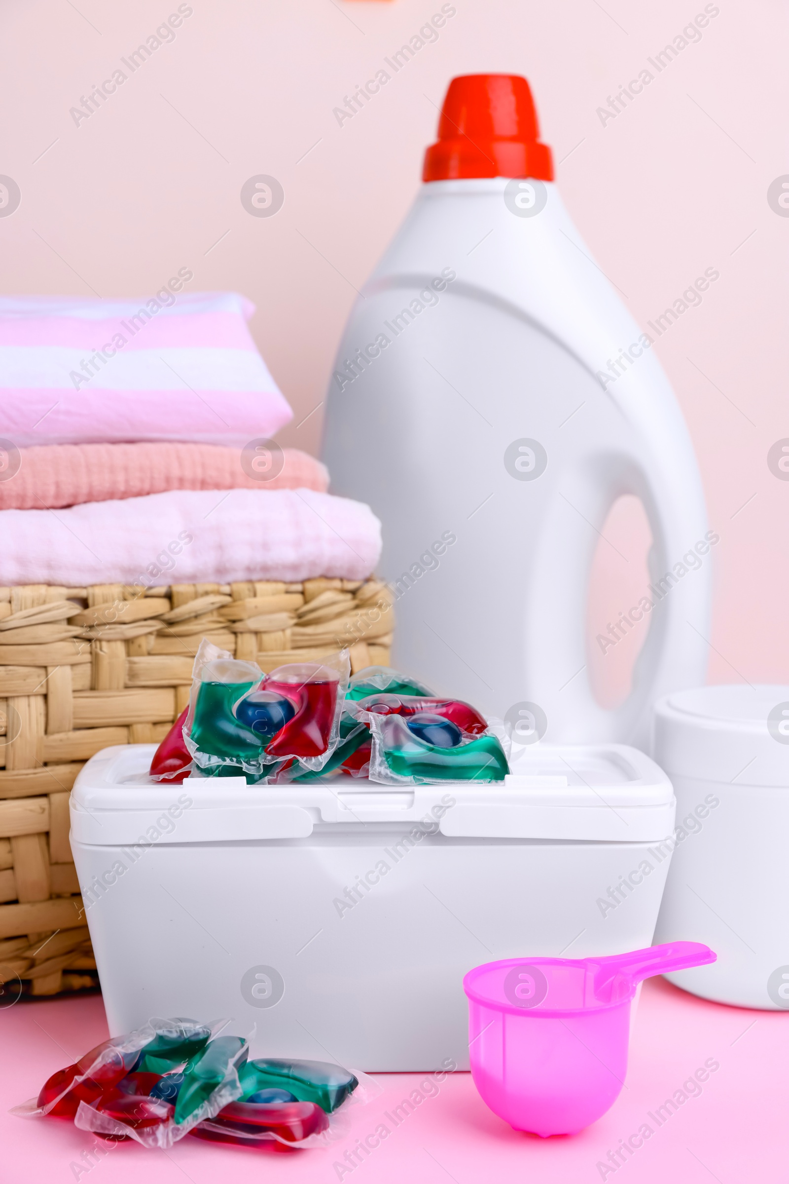 Photo of Laundry capsules, detergent and clean linens on pink table, closeup