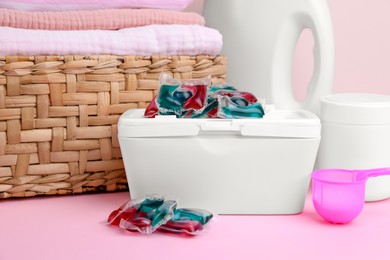 Photo of Laundry capsules, detergent and clean linens on pink table, closeup