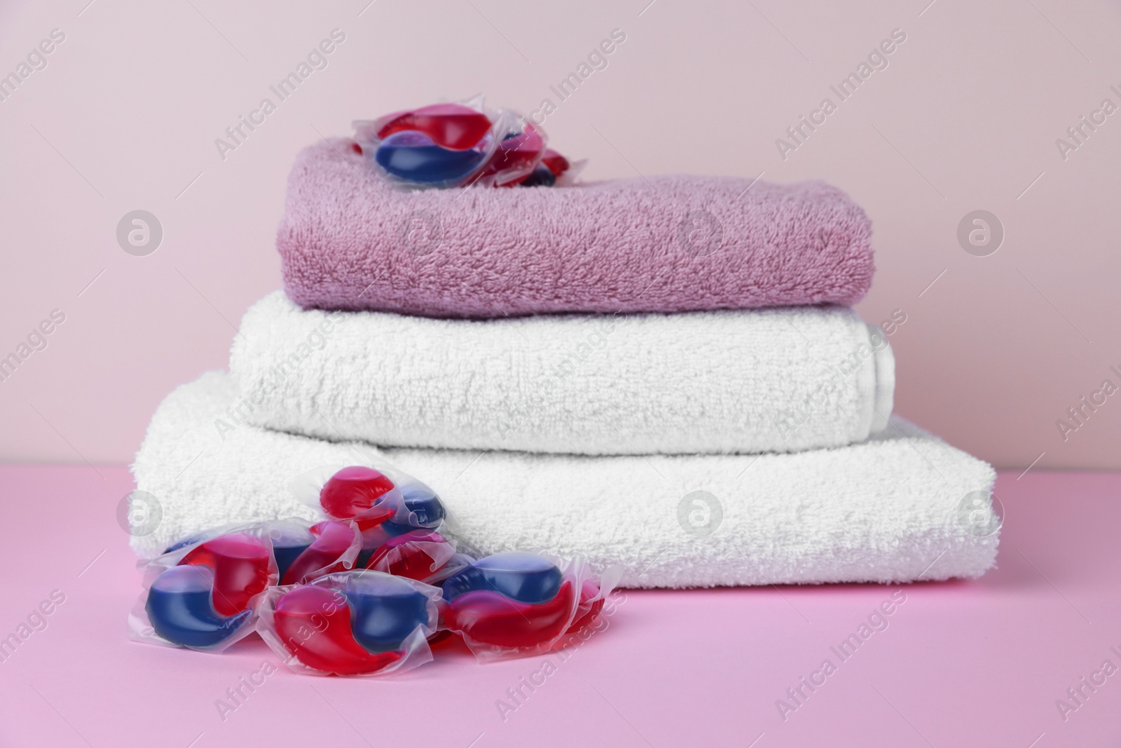 Photo of Laundry detergent capsules and clean towel on pink background