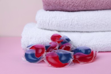 Photo of Laundry detergent capsules and clean towel on pink background, closeup