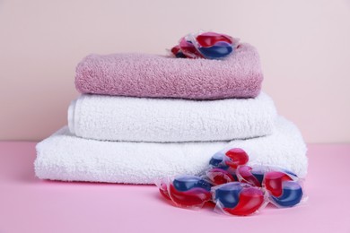 Photo of Laundry detergent capsules and clean towel on pink background