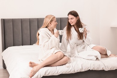 Photo of Spa day. Beautiful women in bathrobes having tea together on bed indoors