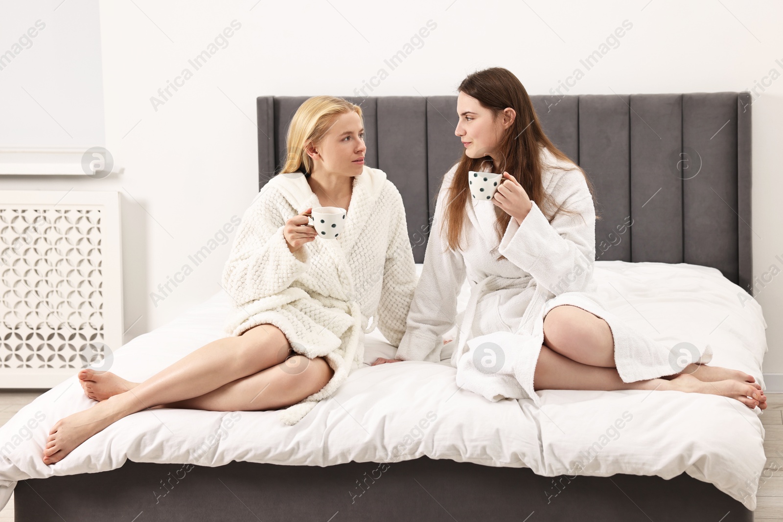 Photo of Spa day. Beautiful women in bathrobes having tea together on bed indoors