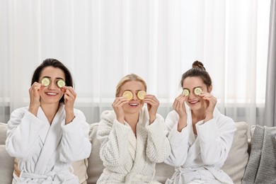 Photo of Happy women with cucumber slices on sofa in spa