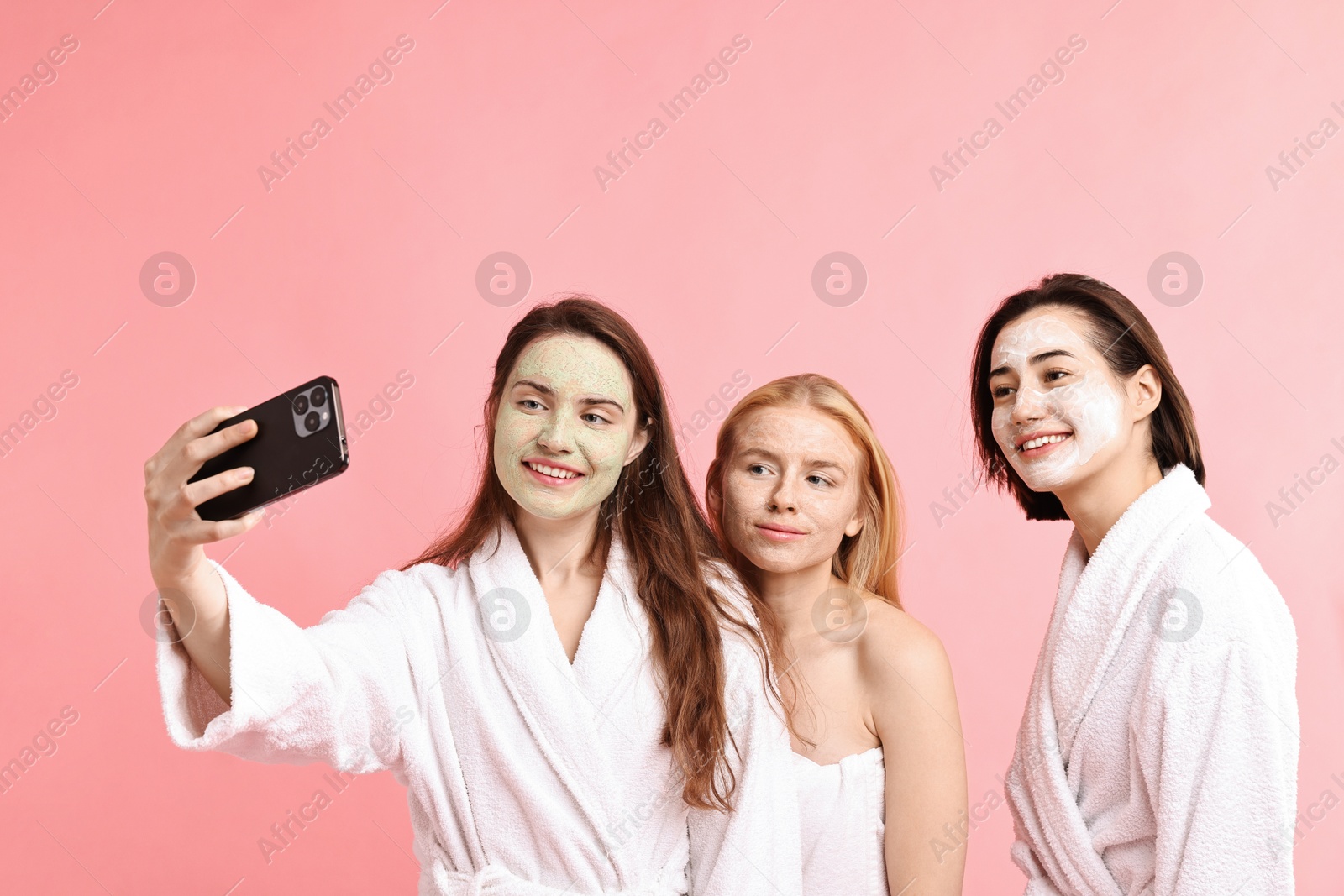 Photo of Spa day. Happy women with face masks taking selfie on pink background