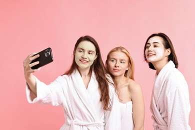 Photo of Spa day. Happy women with face masks taking selfie on pink background