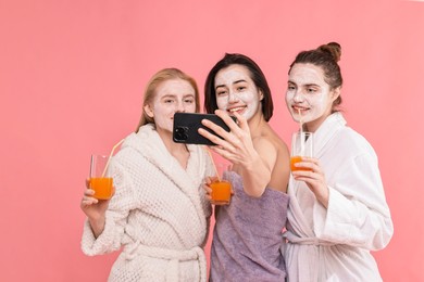 Photo of Spa day. Beautiful women with face masks and healthy drinks taking selfie on pink background