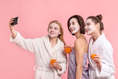 Photo of Spa day. Beautiful women with face masks and healthy drinks taking selfie on pink background