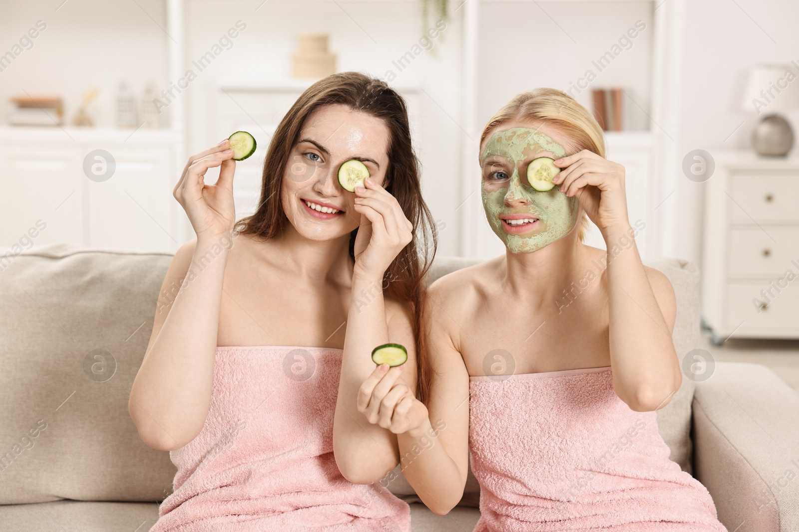 Photo of Spa day. Beautiful women with face masks and cucumber slices on sofa indoors