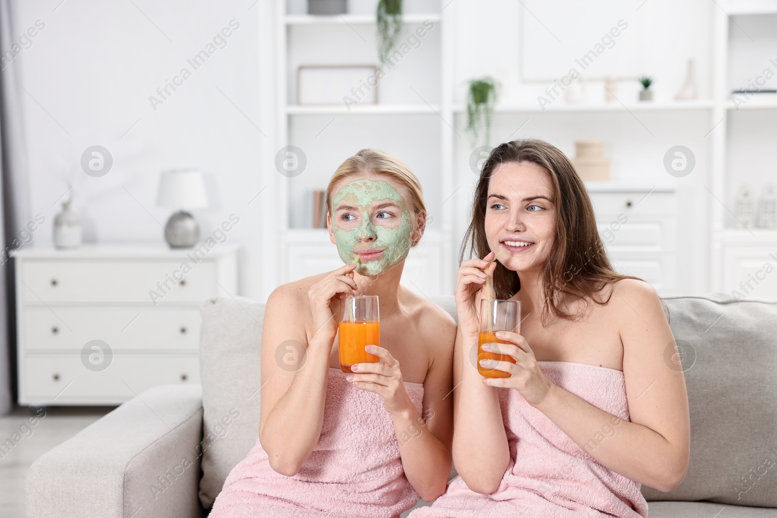 Photo of Spa day. Beautiful women with face masks and healthy drinks on sofa indoors