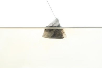 Photo of Putting tea bag into glass cup on white background, closeup