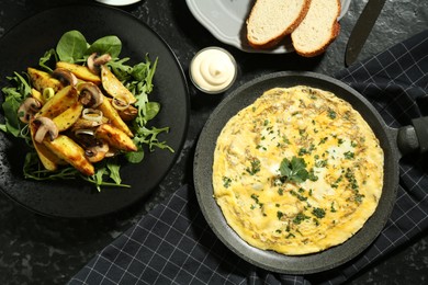 Photo of Tasty brunch. Delicious omelette and fried potatoes served on black textured table, flat lay