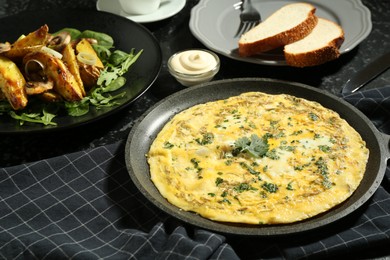 Photo of Tasty brunch. Delicious omelette and fried potatoes served on black textured table