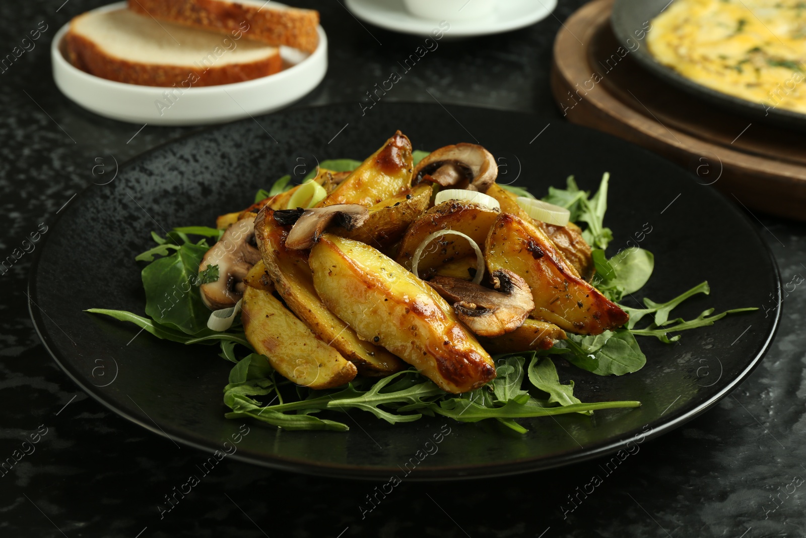 Photo of Tasty brunch. Delicious fried potatoes with arugula and mushrooms served on black textured table, closeup