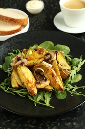 Photo of Tasty brunch. Delicious fried potatoes with arugula and mushrooms served on black textured table, closeup