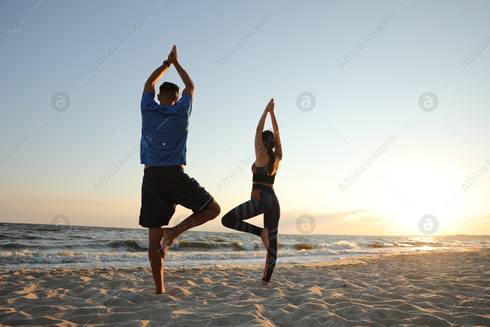 Photo of Couple doing yoga on beach at sunset